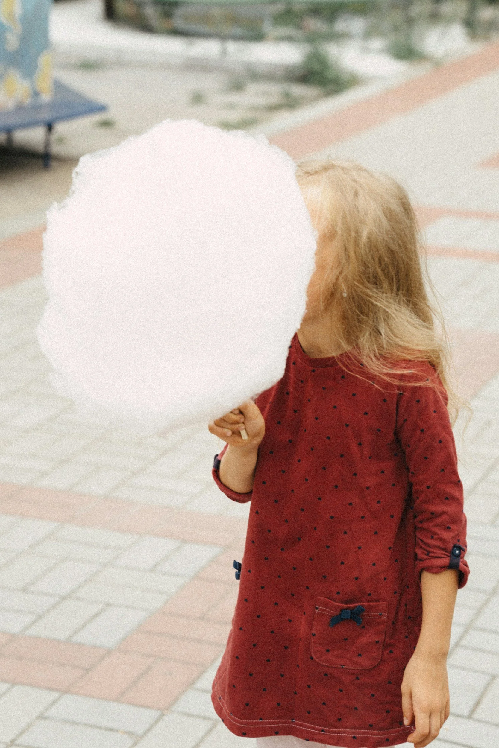 A girl holding a large white cotton candy on a stick.