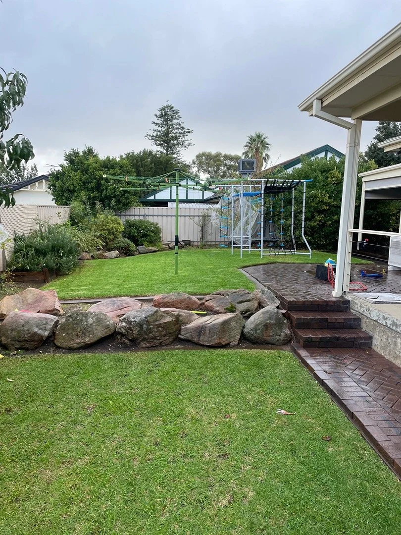 A backyard with a lawn, rocks, a clothesline, a playground structure, and outdoor steps leading to a porch.