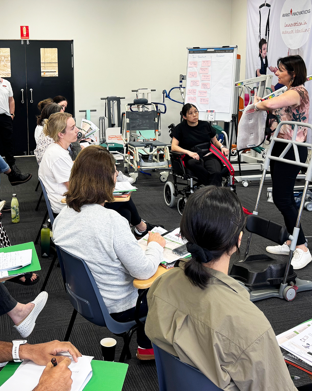 A woman demonstrating at a seminar about medical devices to an audience in a classroom setting.