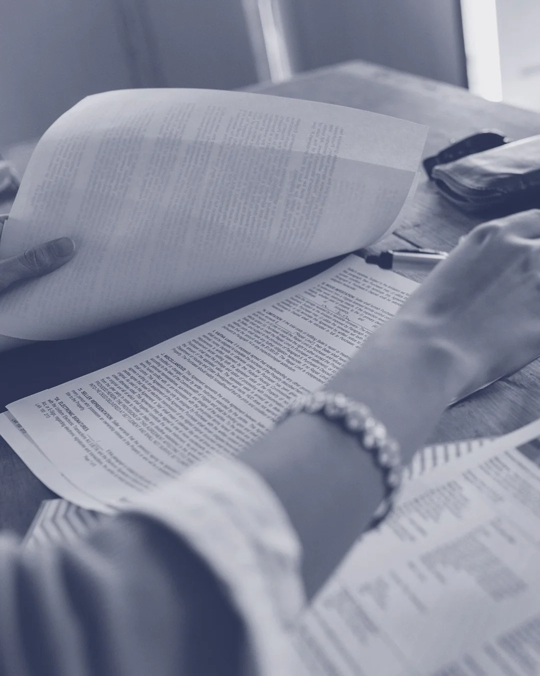 Person reading printed documents on a desk with a pen and a wallet nearby.