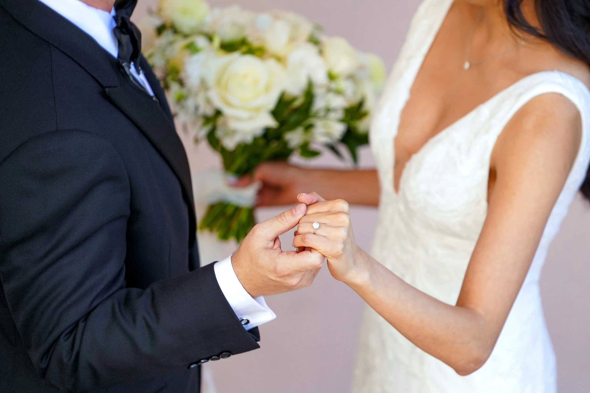 Close-up of a groom holding the bride’s hand to show her diamond engagement ring during a wedding portrait.