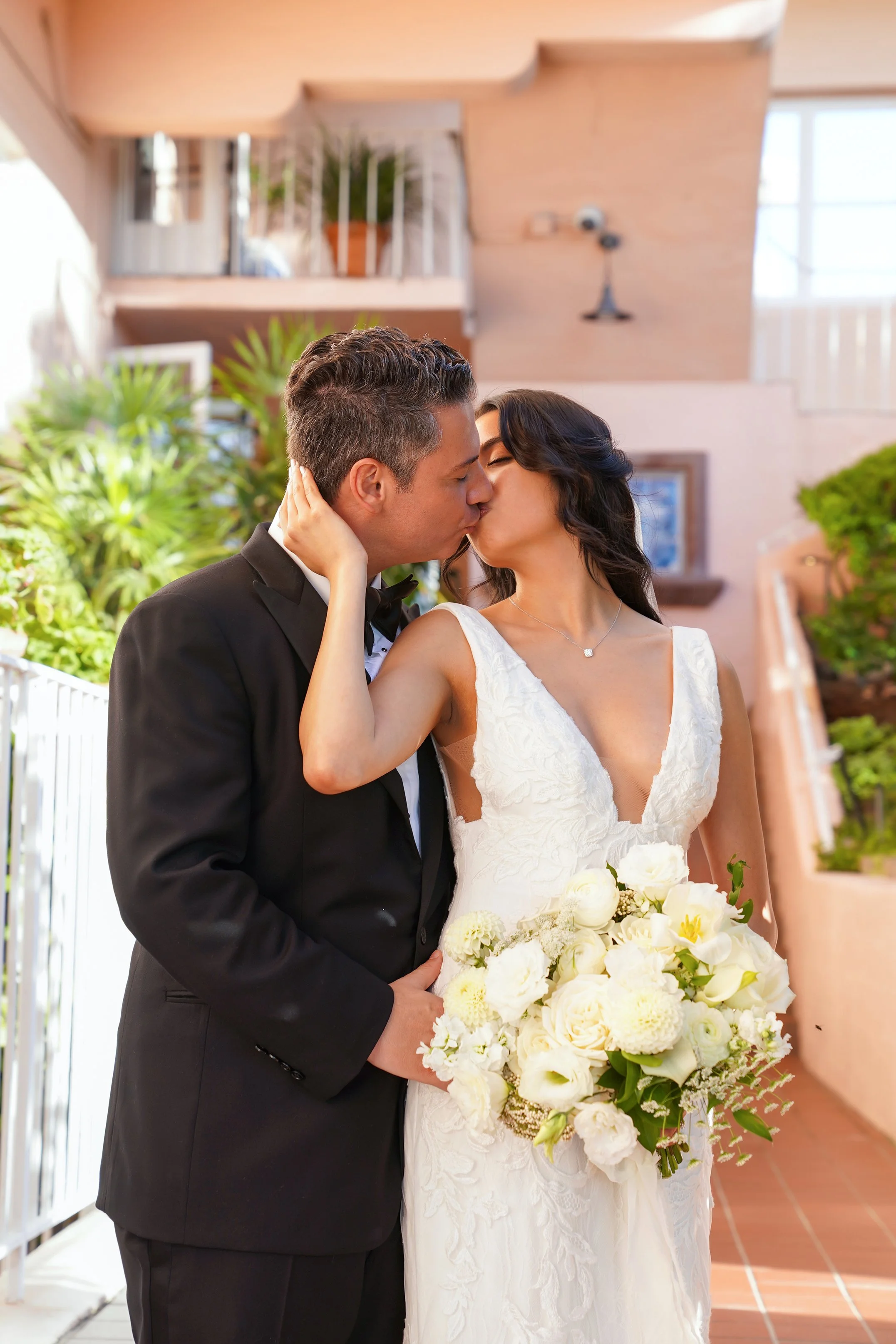 Bride and groom kissing while holding a white rose and ranunculus bouquet during their wedding portraits at La Valencia Hotel in La Jolla, San Diego.