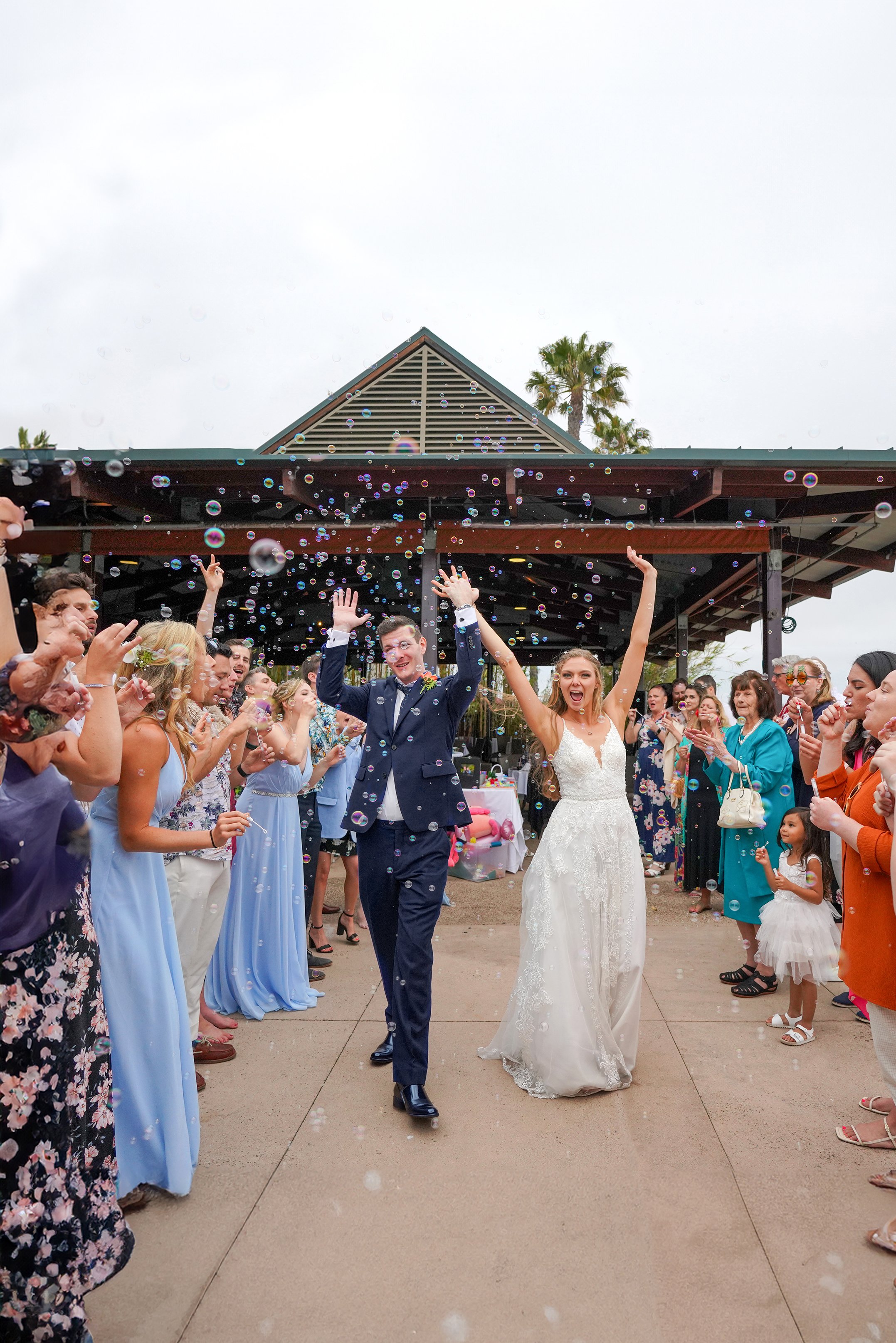 candid wedding exit photo captured by Reimo Photography a San Diego wedding photographer showing happy bride and groom walking through guest blown bubbles.