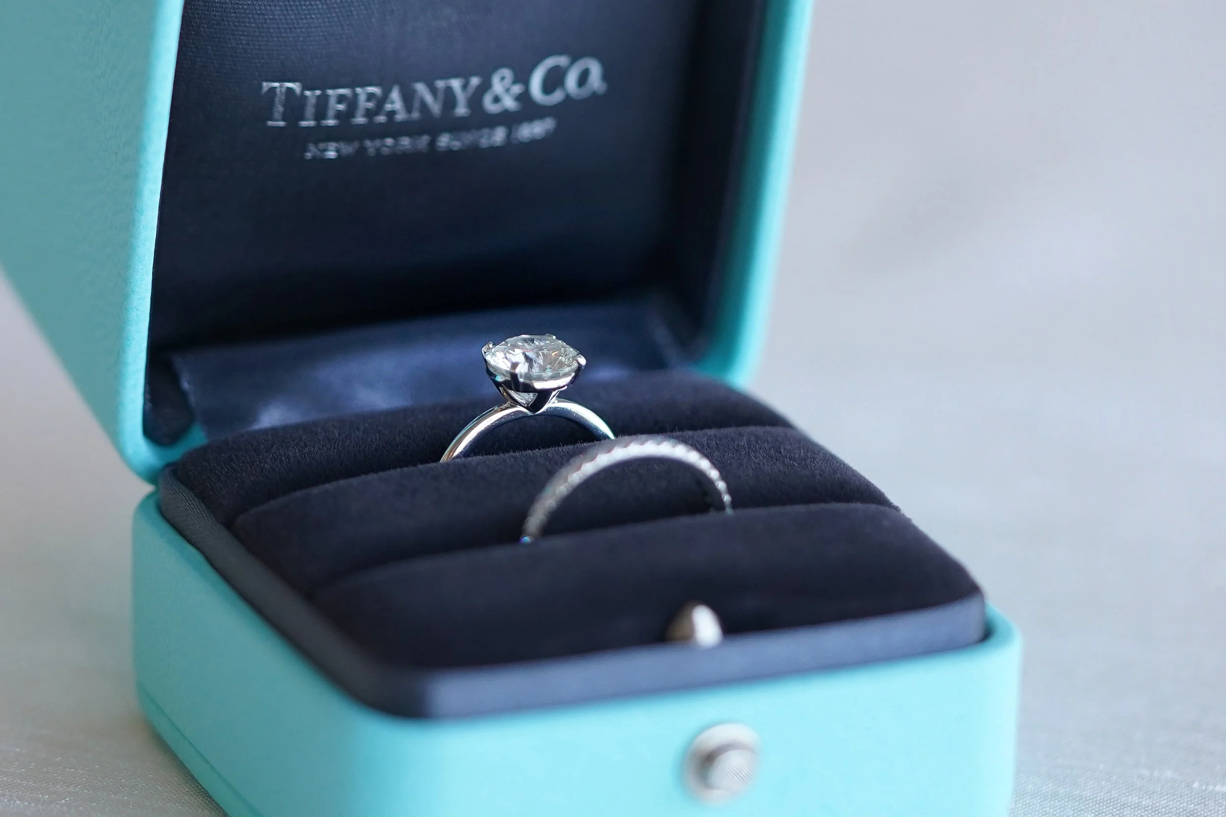 Tiffany and Co round brilliant cut diamond engagement ring and matching pavé wedding band displayed inside an open classic blue Tiffany ring box.