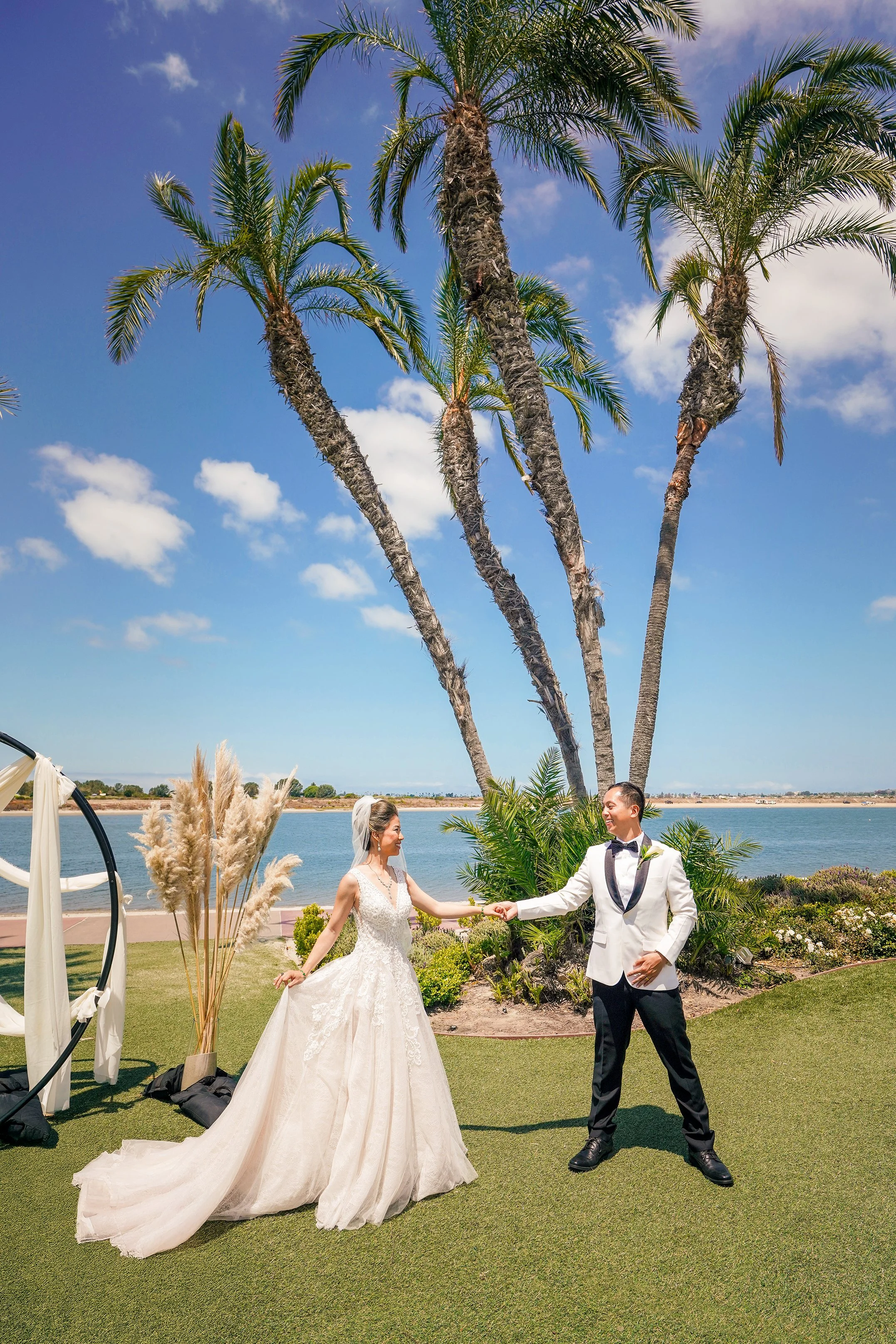 Bride and groom holding hands under tall palm trees at a waterfront wedding ceremony at San Diego Mission Bay Resort.