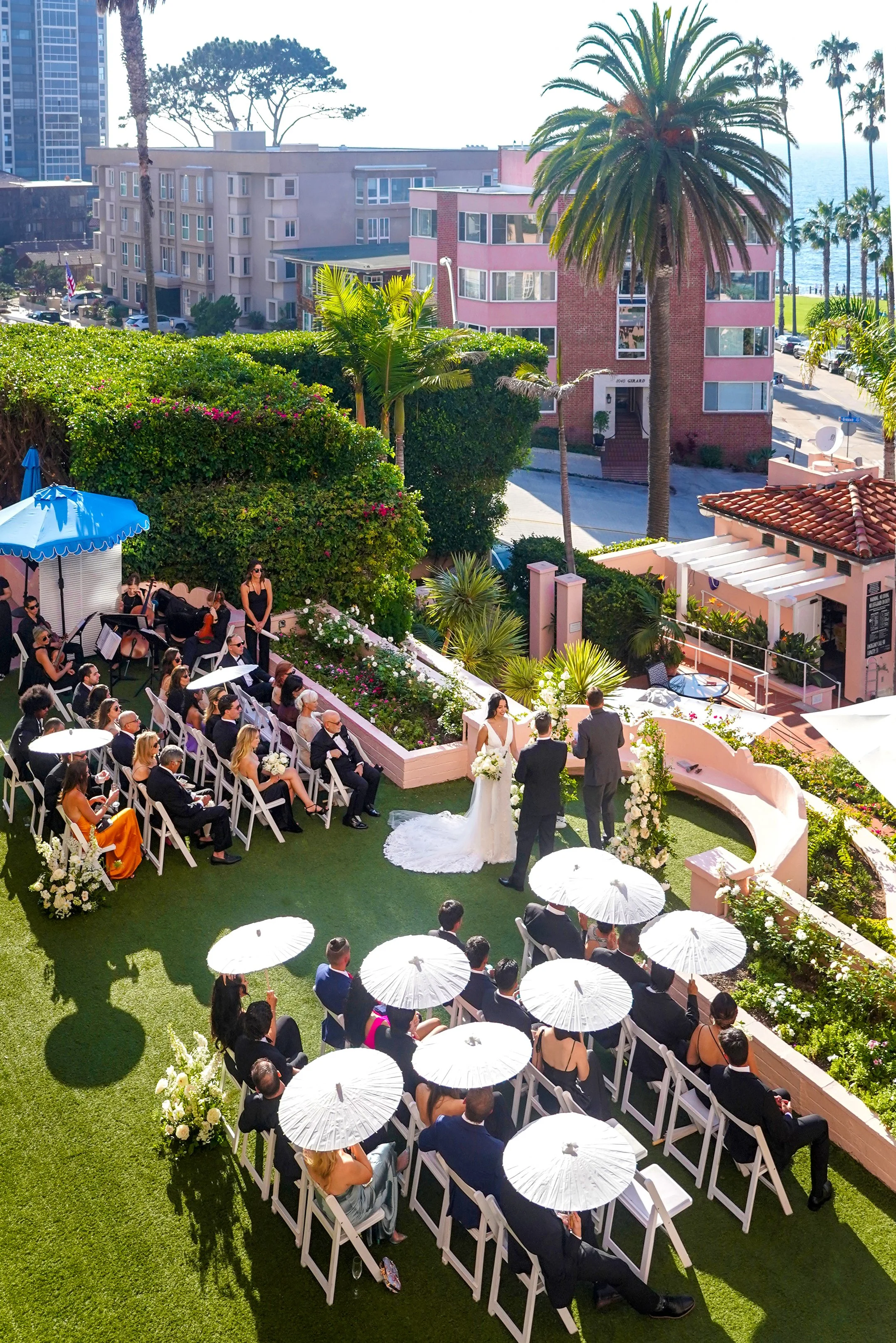 Outdoor garden lawn wedding ceremony at La Valencia Hotel in La Jolla San Diego featuring white parasols and ocean views.