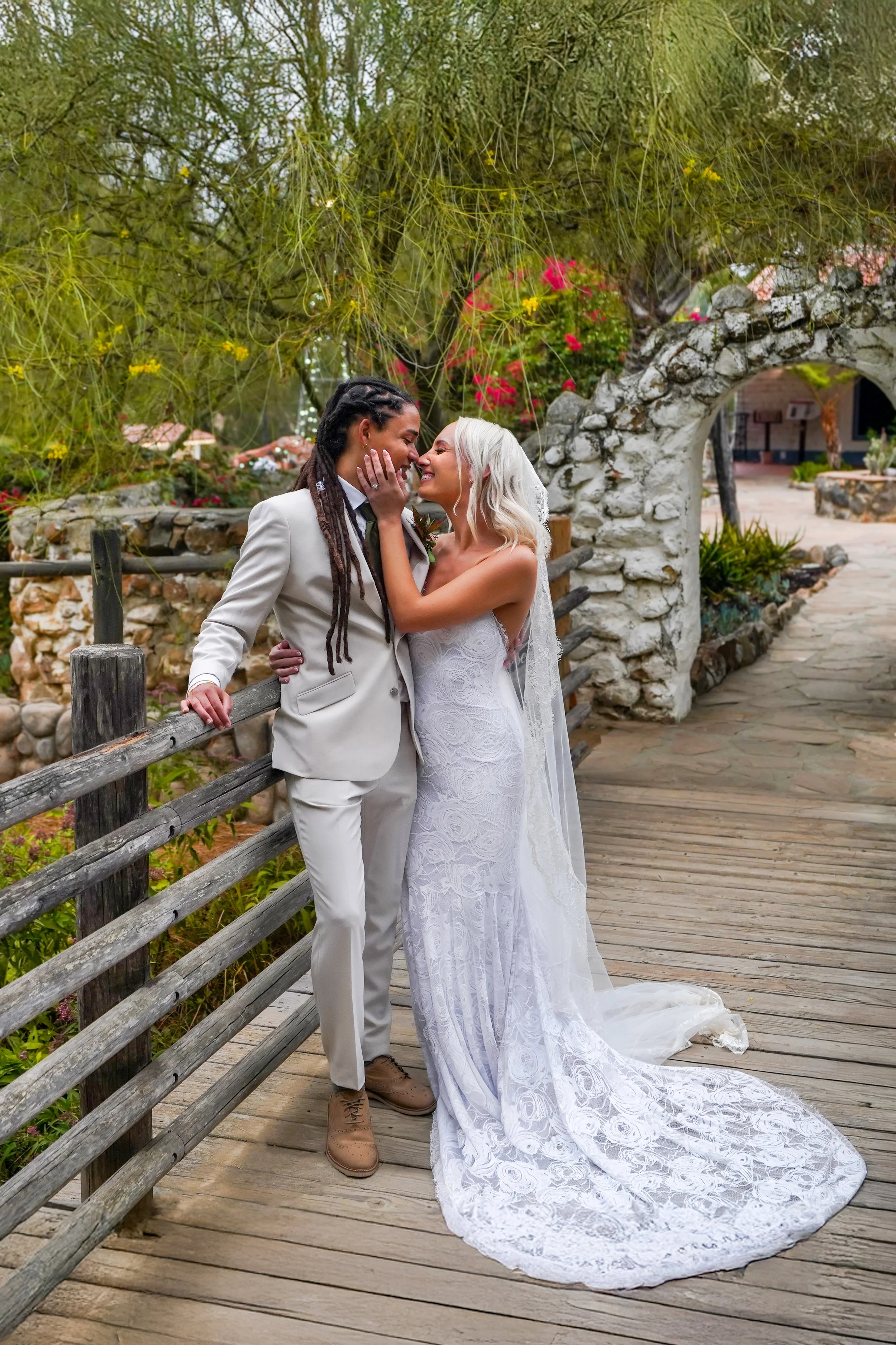 Candid, fine art wedding portrait of a bride in a lace gown and a groom in a beige suit sharing an intimate moment on a rustic wooden bridge at Leo Carrillo Ranch Historic Park in Carlsbad, San Diego.