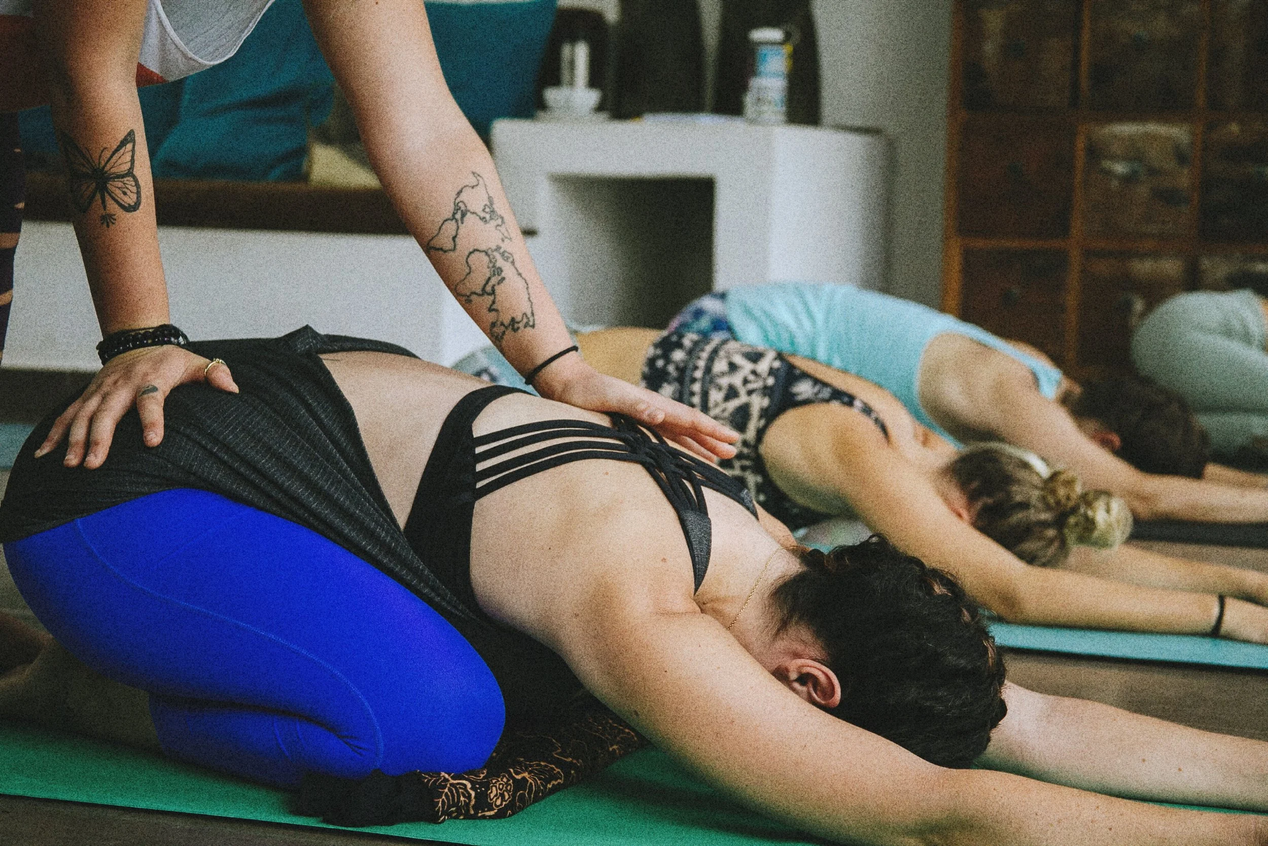Multiple people practicing yoga in a studio, person in foreground wearing blue leggings, performing downward dog pose, others in similar poses in background.