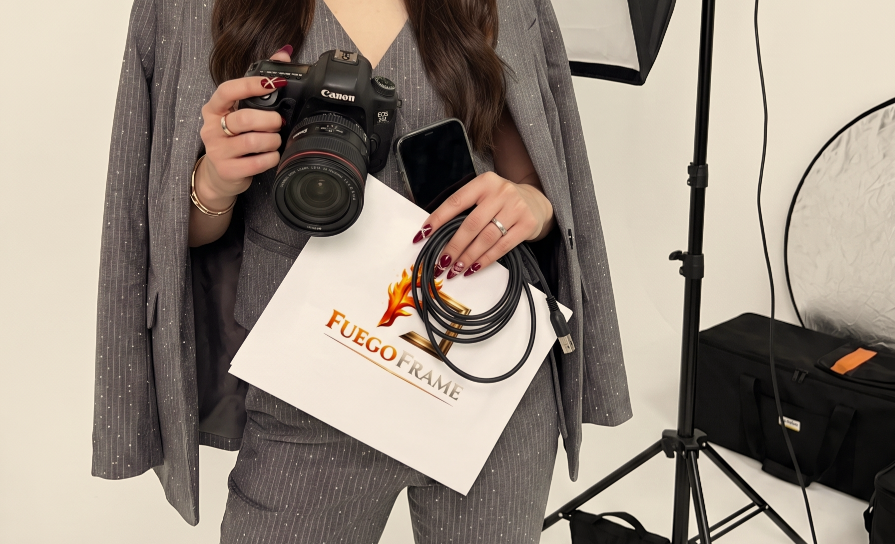 Woman in a pinstripe suit holding a camera and phone in a branded Fuego Frame Media studio setup.