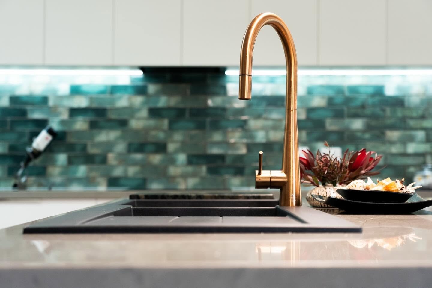 Kitchen sink with a copper faucet, decorative plants, and bowls of shells on a countertop, with a backsplash of multicolored tiles.