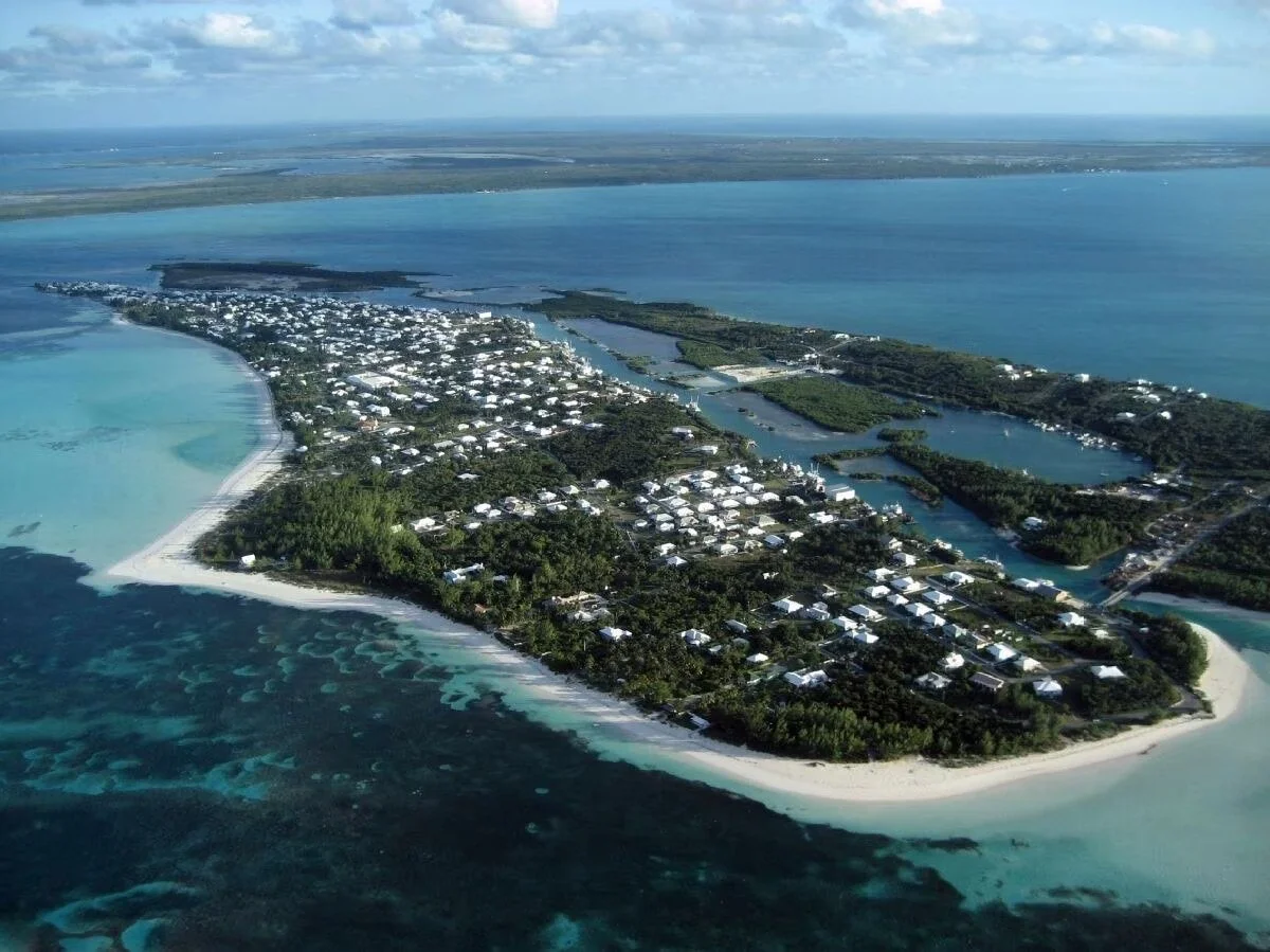 Aerial view of a coastal island with buildings, narrow waterways, sandy beaches, and surrounding turquoise ocean waters during daytime.
