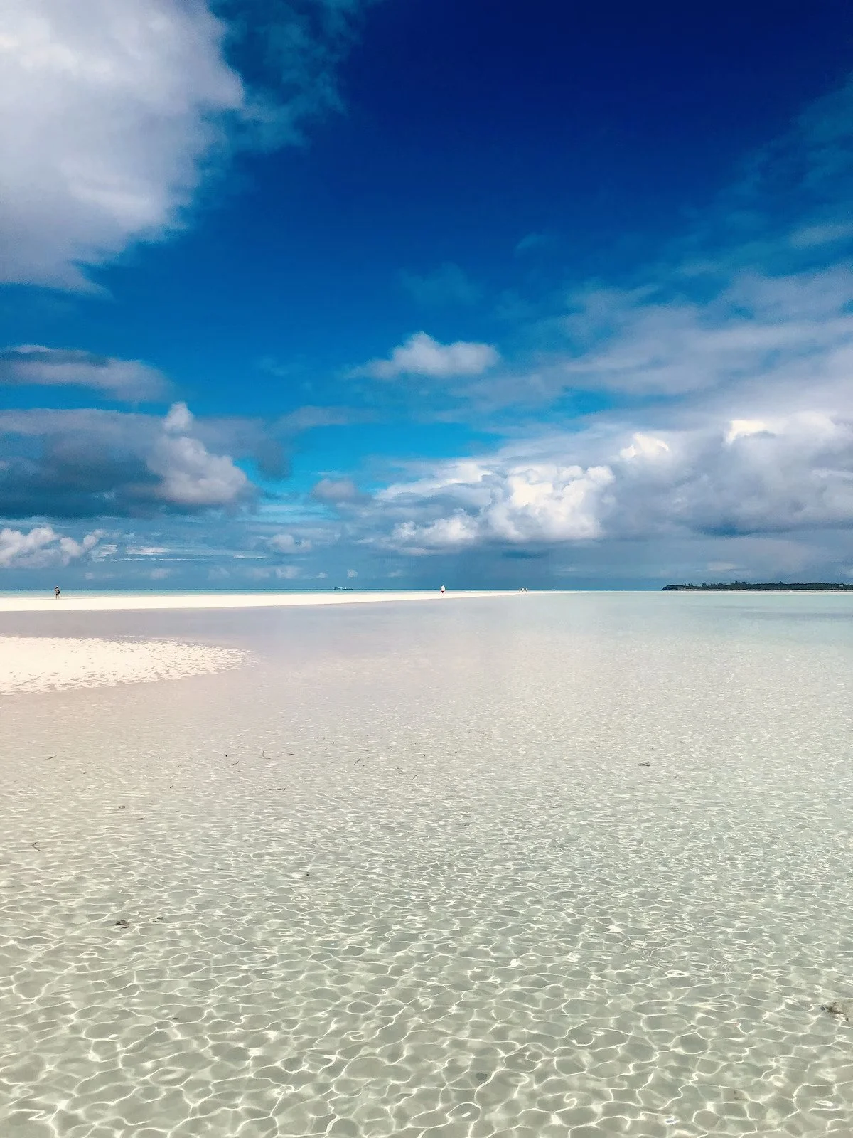 White sandy beach with a deep blue sky and clouds, and a distant shoreline.