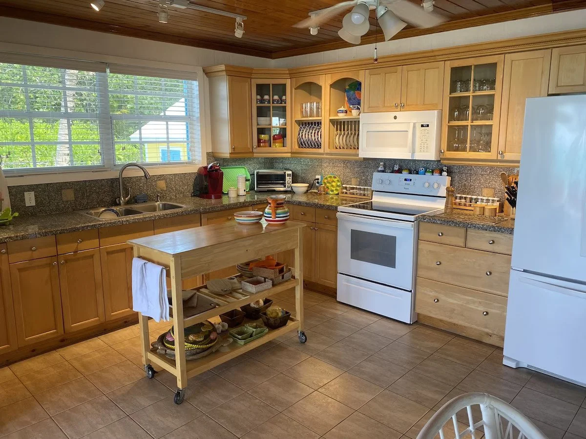 Kitchen with wooden cabinets, granite countertops, white appliances, a window with blinds, and a wooden kitchen island on wheels.