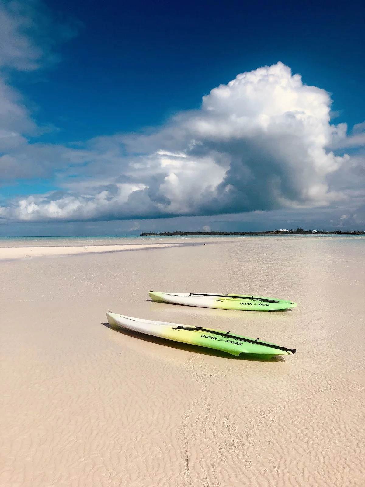 Two yellow and white kayaks on a sandy beach under a partly cloudy sky with distant land and calm water.