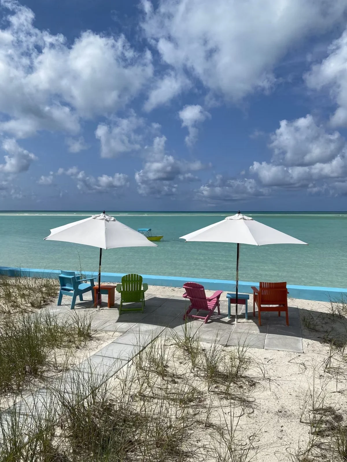 Colorful beach chairs with umbrellas on sandy beach overlooking turquoise water and blue sky with clouds.