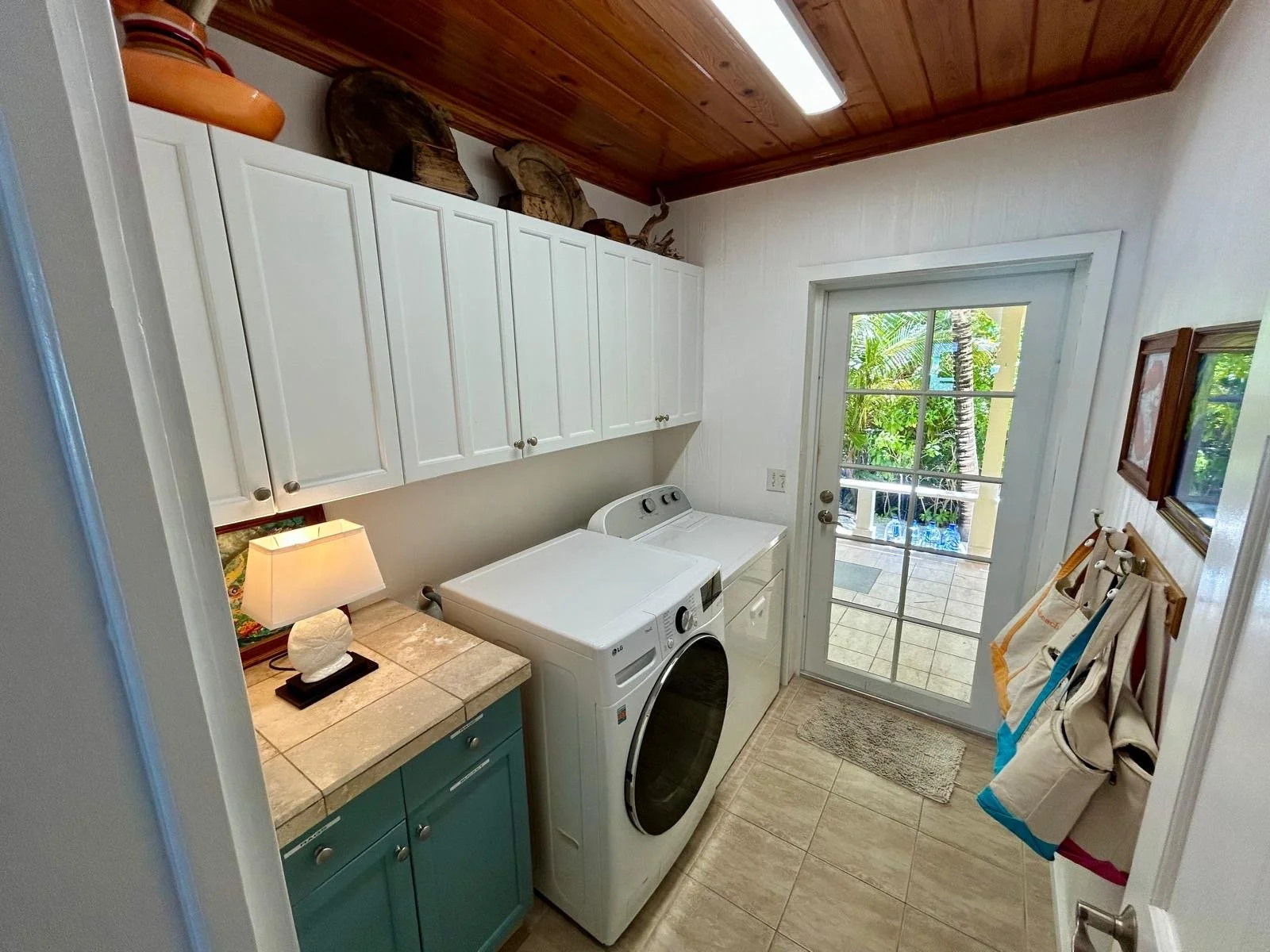 Laundry room with washer and dryer, white upper cabinets, a countertop with a lamp, a door leading outside, and laundry bags hanging on the wall.