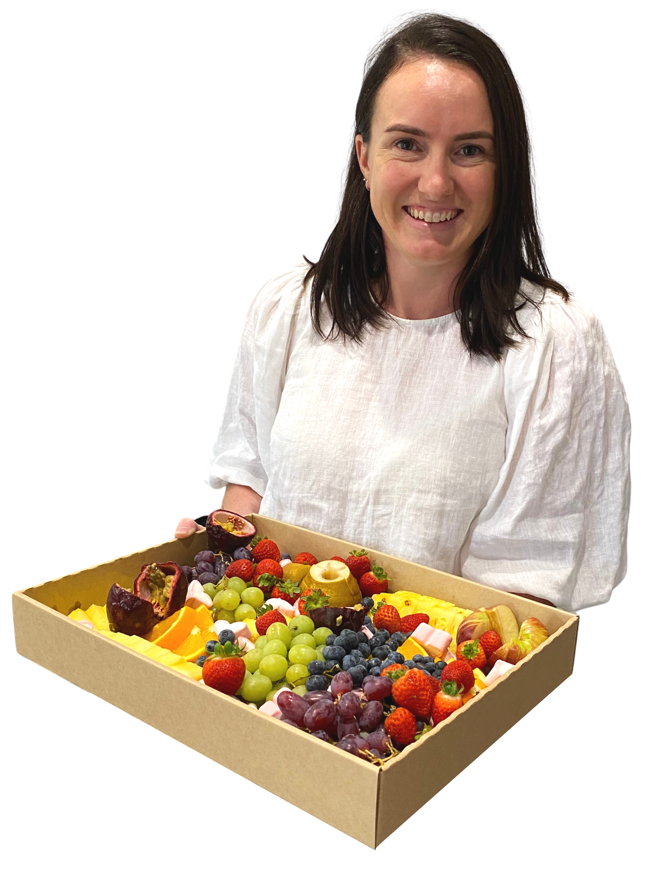A woman with dark hair smiling, holding a large tray of colorful assorted fresh fruits, including strawberries, grapes, pineapple, and passion fruit.