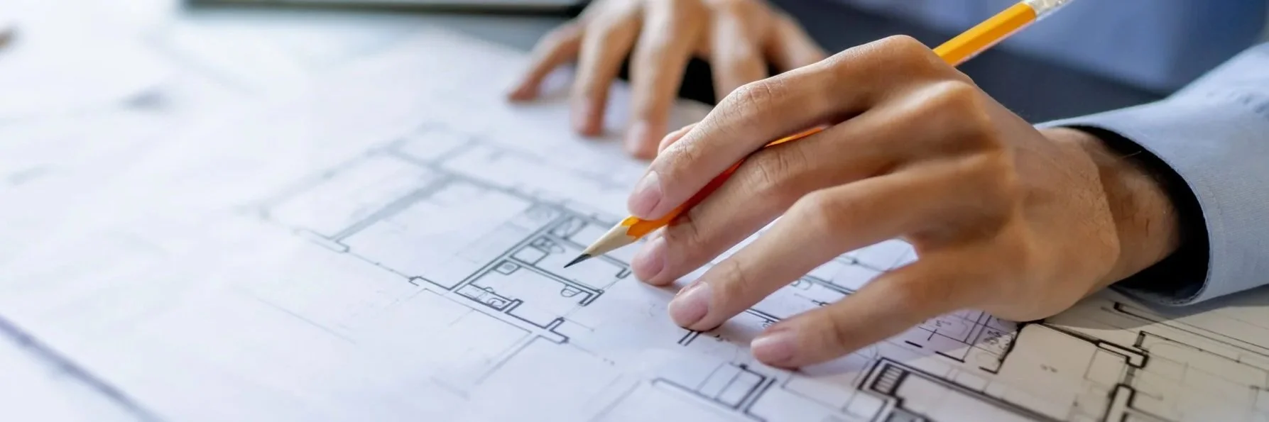 Hand of a person in a suit drawing a building blueprint with a pencil on desk.