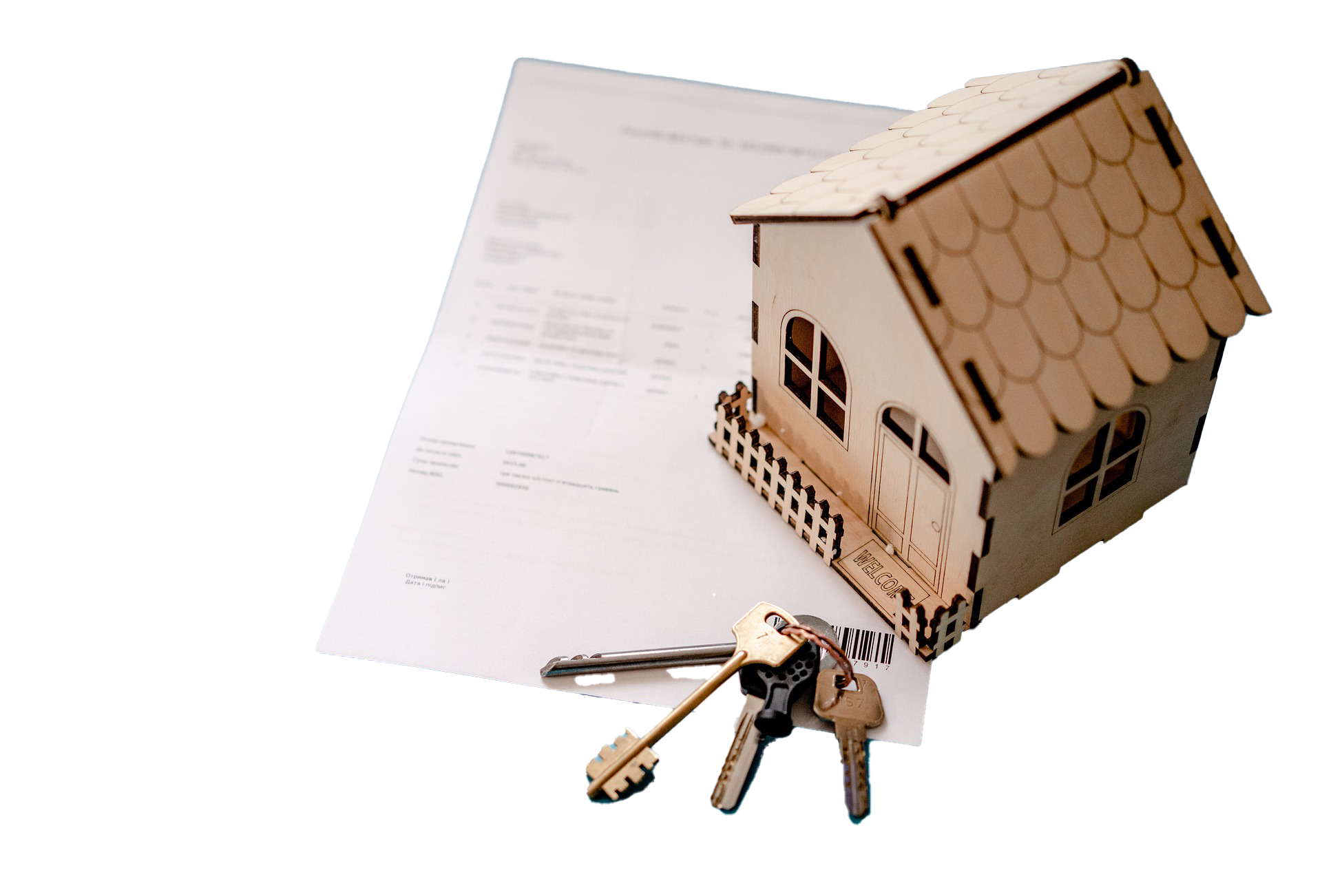 A small wooden house model placed on top of a sheet of paper, with a set of keys and a keychain in the foreground.