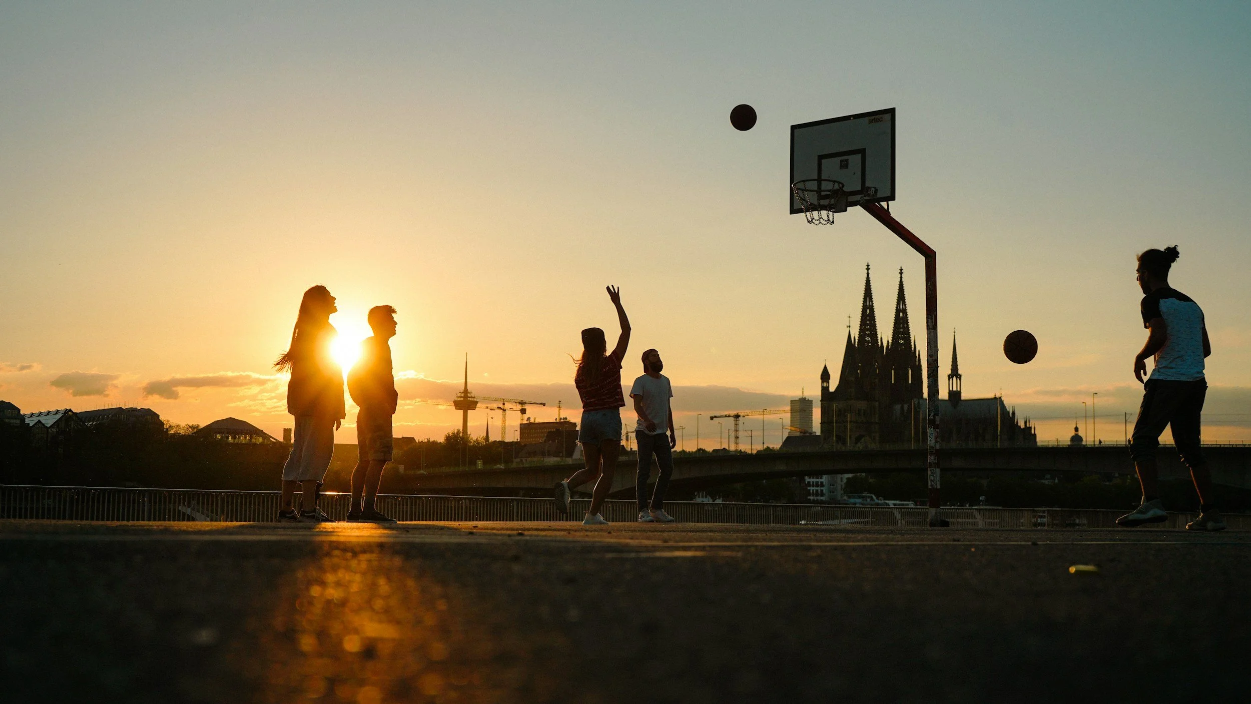 Silhouettes of children playing basketball during sunset with a church in the background.