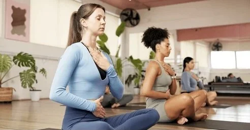 Women practicing meditation or yoga in a spacious indoor studio.