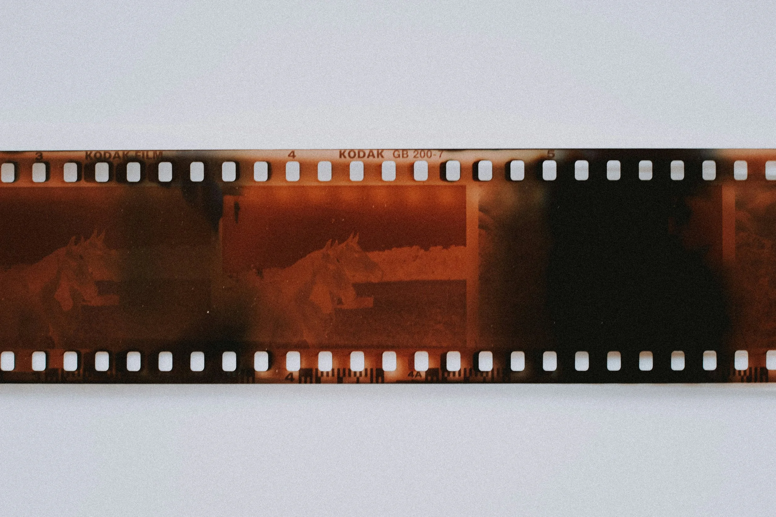 Close-up of a strip of Kodak film with perforations, placed on a white surface.
