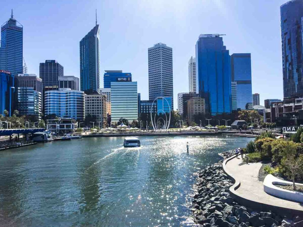 View of a city skyline with high-rise buildings, a waterfront, and a boat on the water during daytime.