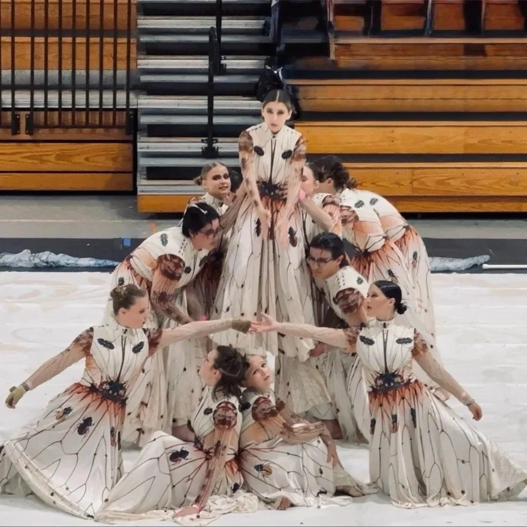 A group of performers dressed in butterfly-themed costumes posing on a gymnasium floor.