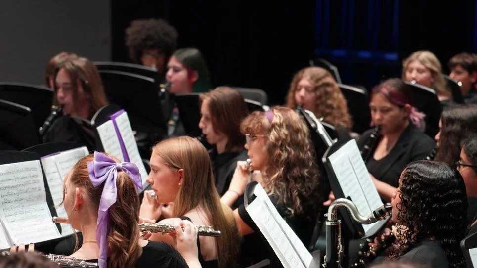Orchestra with female musicians playing instruments, some holding flutes and clarinets, during a performance.