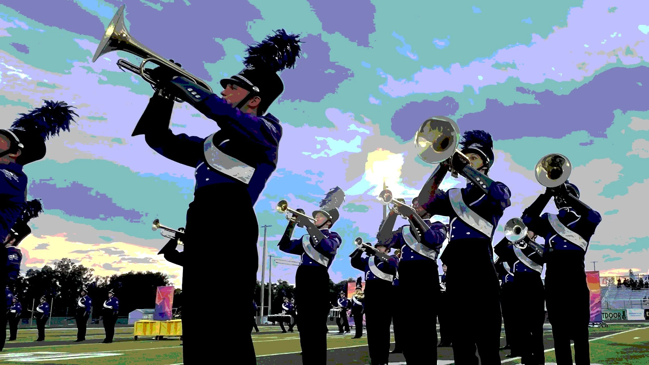 A marching band performing outdoors at sunset, with members dressed in blue uniforms and wearing plumed hats, playing brass instruments.
