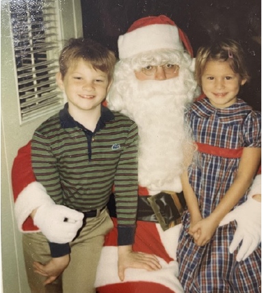 Two children, a boy and a girl, posing with Santa Claus in a festive setting.