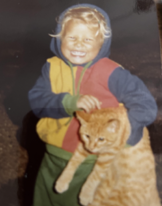 A young child smiling and holding a large orange tabby cat outdoors.