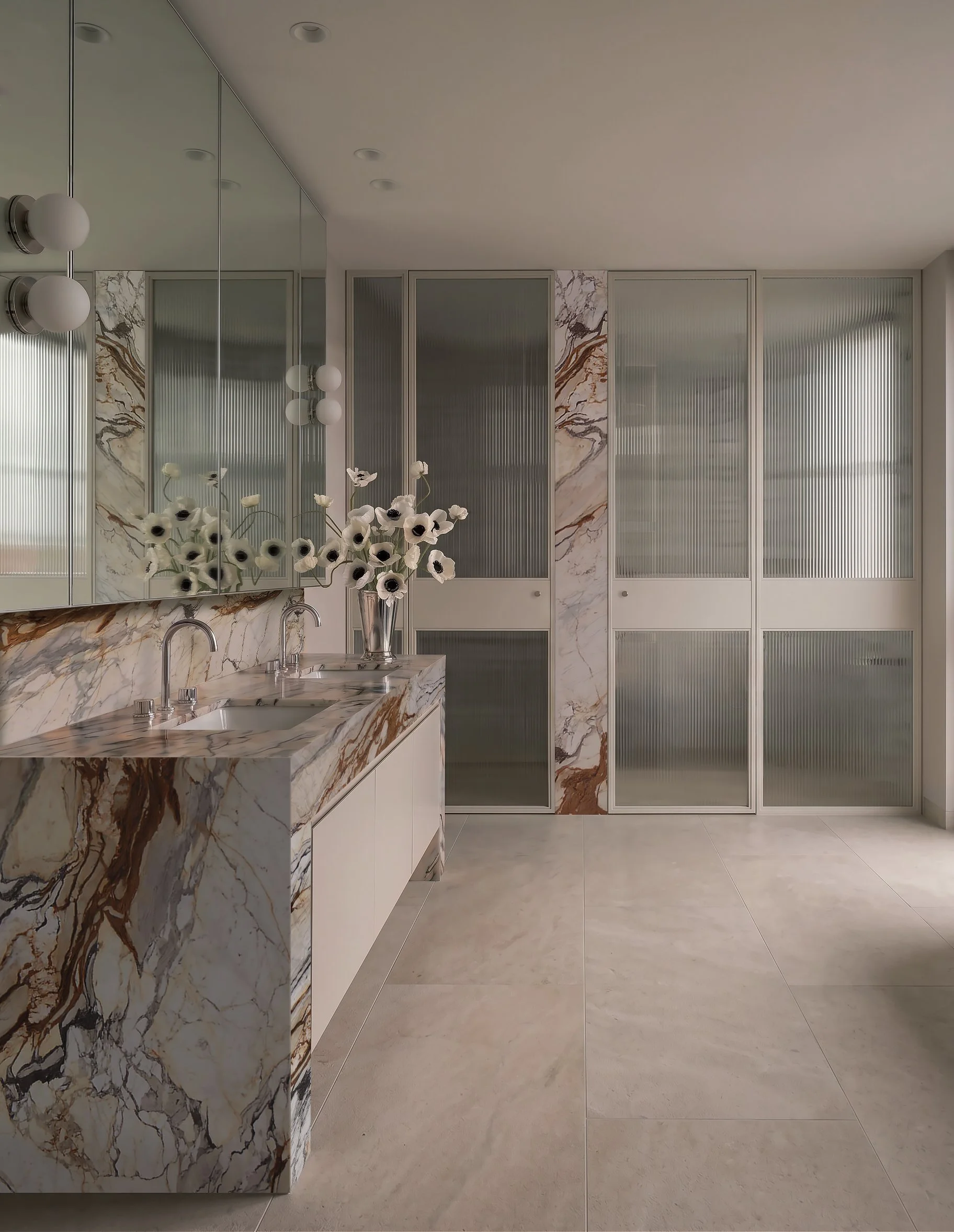 A modern bathroom with marble countertops and backsplash, a large mirror, wall-mounted light fixtures, and frosted glass panel cabinet doors, with beige floor tiles.