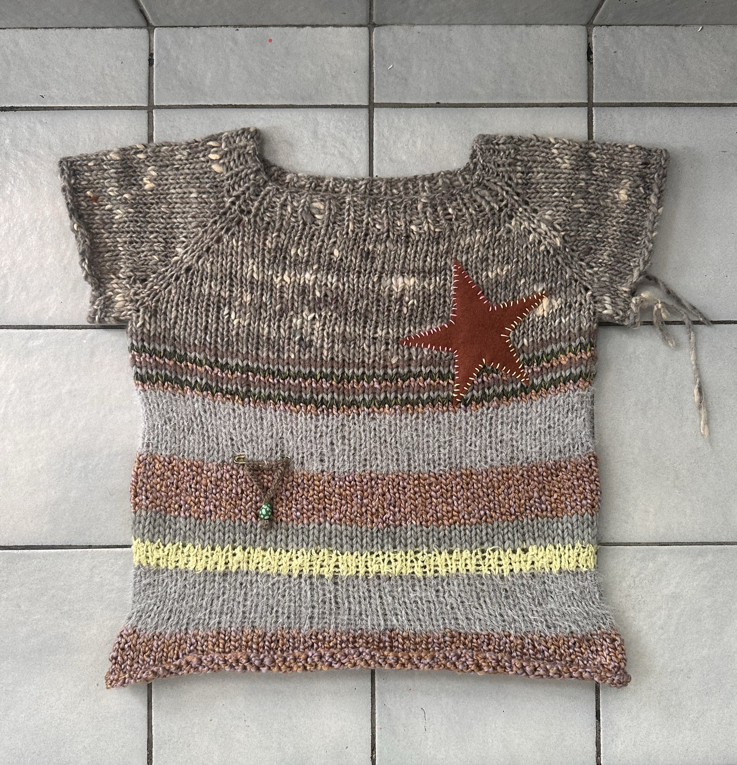 A multi-colored woven wool sock with a red star design on the side, laid on a tiled gray floor.