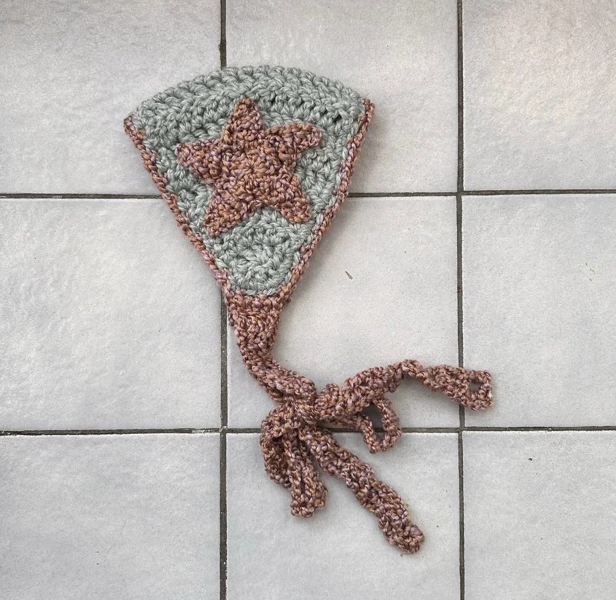 Crocheted flower-shaped item with a star in the center, lying on a tiled floor.