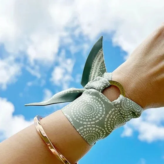 A person holding a dollar bill in their hand, wrapped with a patterned cloth, against a background of a blue sky with clouds.