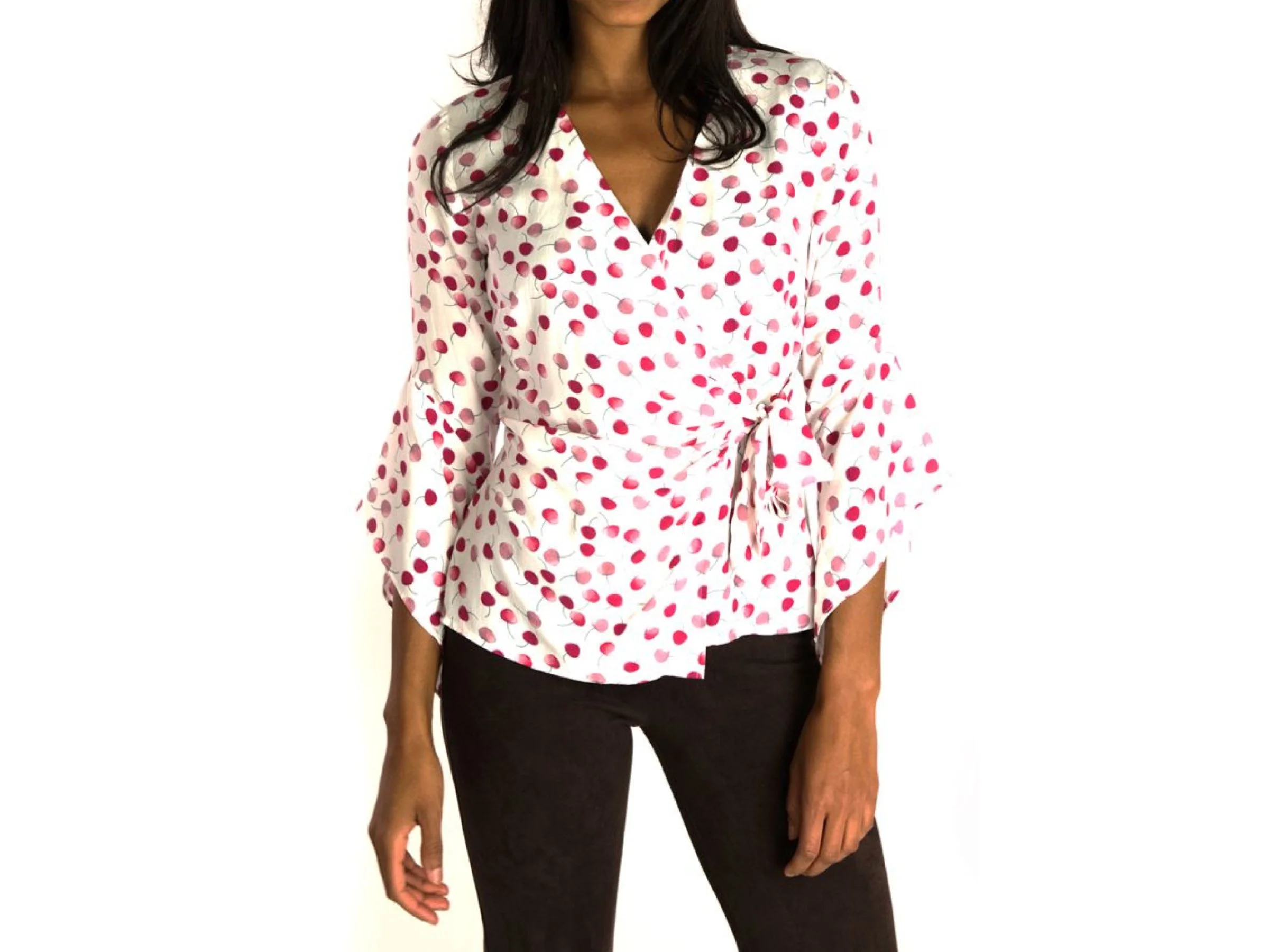 A woman wearing a white blouse with a tossed cherry print and a tie at the waist, and black pants.