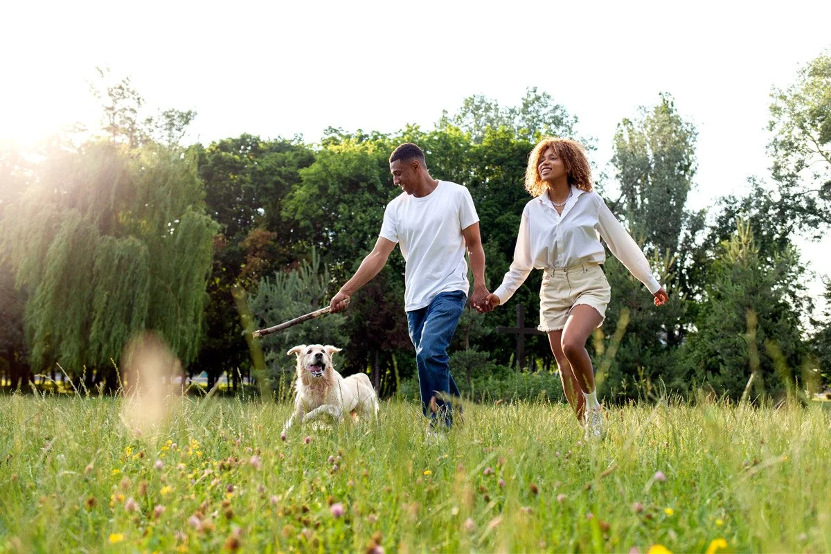 A couple holding hands and playing with a dog in a park during daytime.