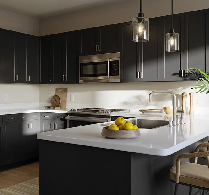 Modern kitchen with dark cabinets, white countertops, stainless steel microwave above stove, and pendant lights. Yellow lemons in a wooden bowl on the island counter at Mill + Miss Apartments in Grand Rapids, MN.