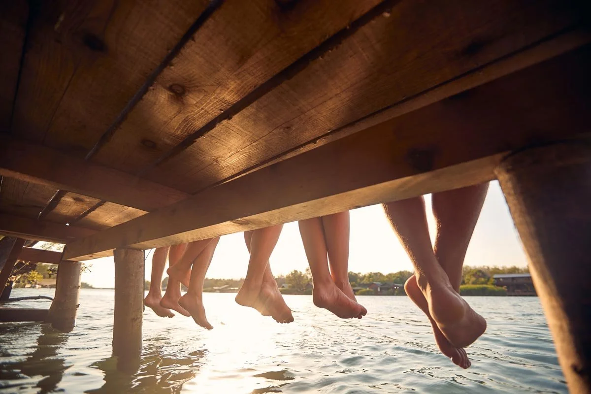 People sitting on a wooden dock with their feet hanging over the water during a sunset.