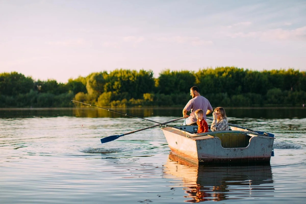 A family of four enjoying a boat ride on a lake during sunset, with a background of trees and calm water.