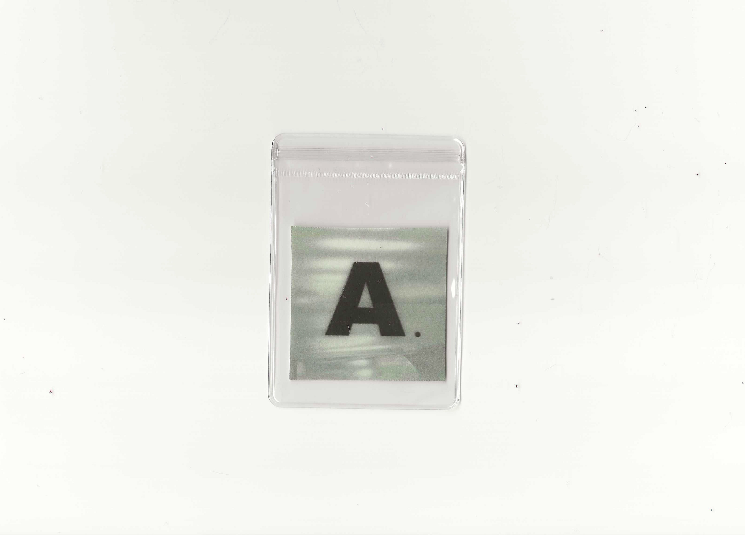 Close-up of a plastic card with the letter 'A' and a period printed on it, encased in a transparent plastic sleeve, placed on a white surface.