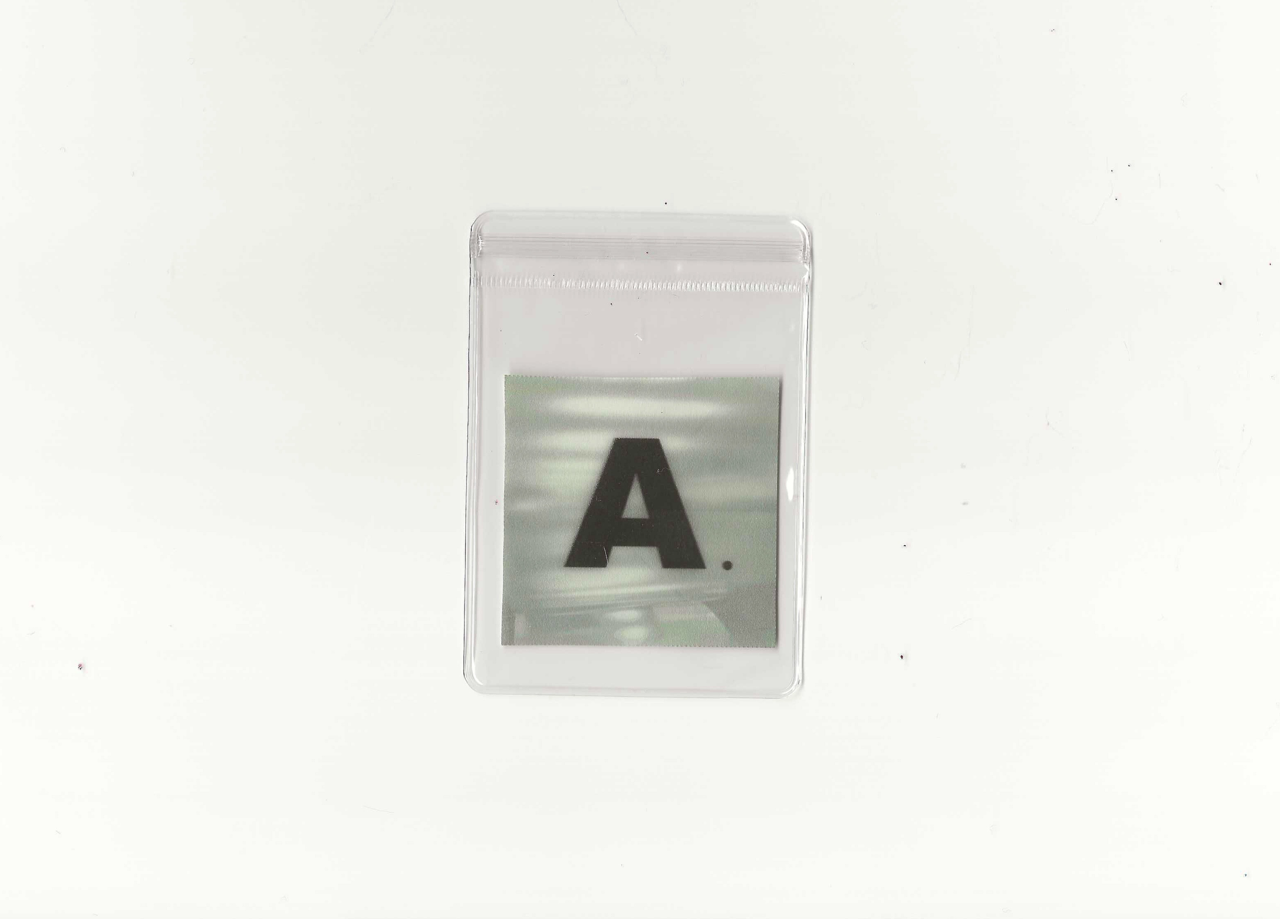 Close-up of a small clear plastic bag with a metallic card inside, displaying a large black letter 'A' on a white background.
