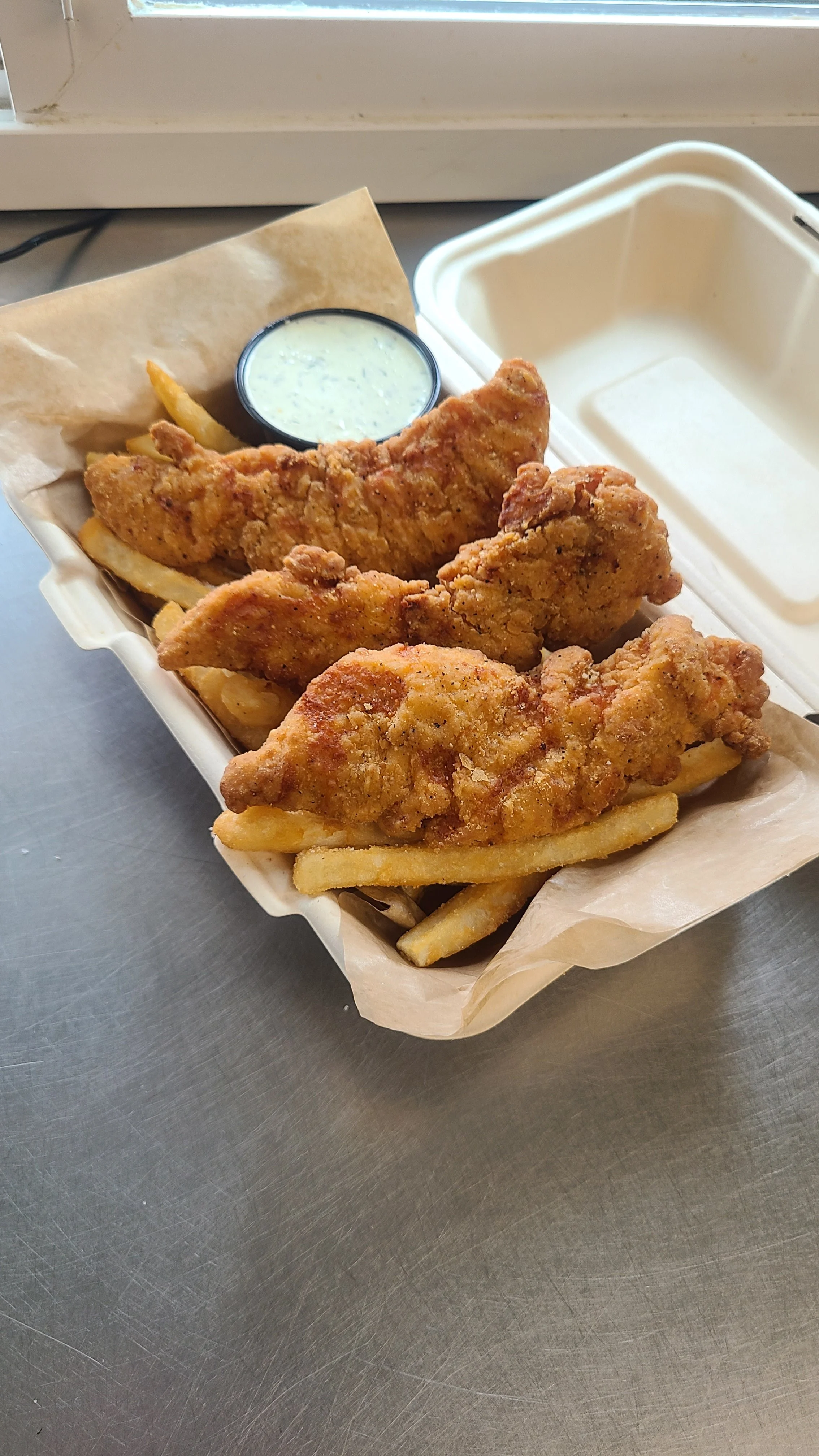 Fried chicken tenders with French fries and a side of ranch dipping sauce in a paper food tray