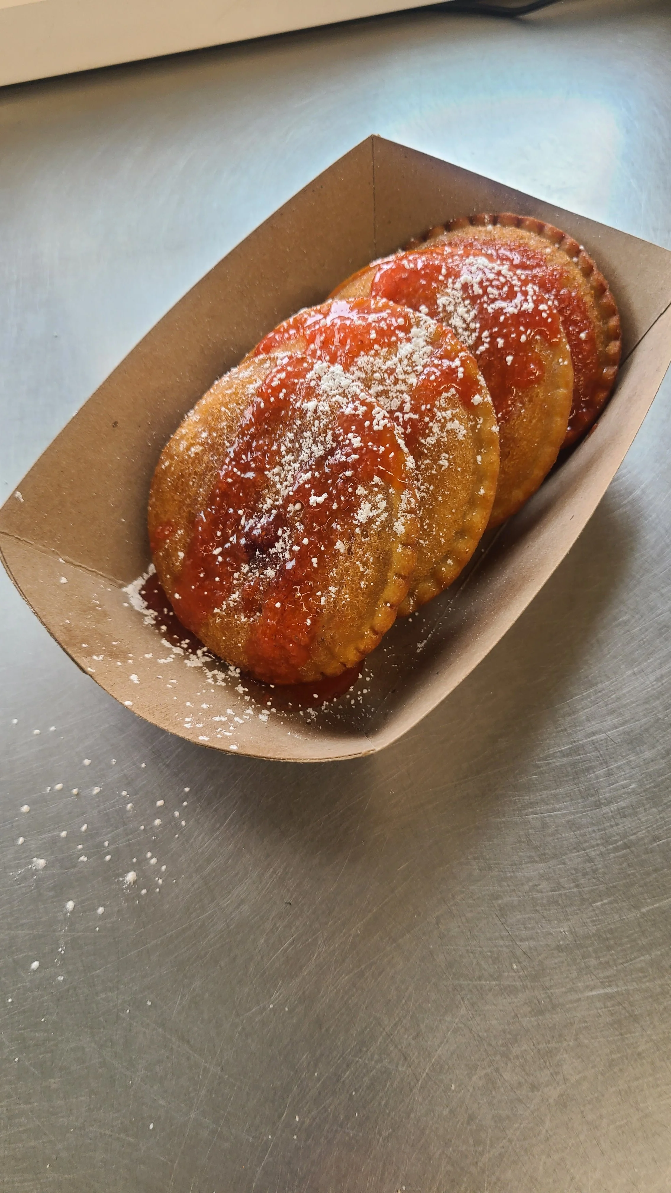Three fried empanadas in a cardboard tray with sauce on top, sprinkled with grated cheese.