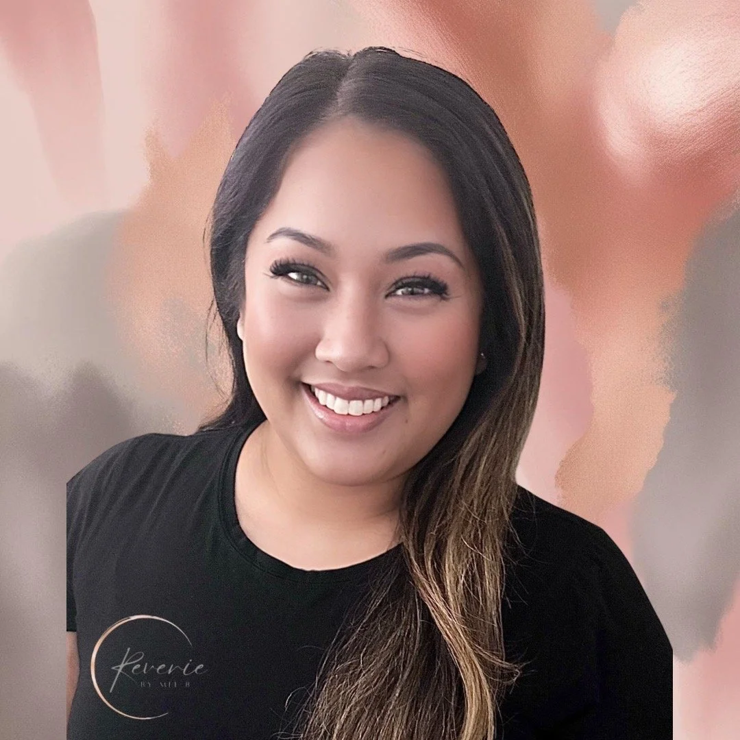 Smiling woman with long dark hair, wearing a black shirt with a logo, standing in front of an abstract pink and beige background.