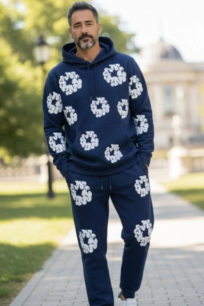 Man walking outdoors in a park, wearing a matching navy hoodie and sweatpants with white floral prints, and grey sneakers.