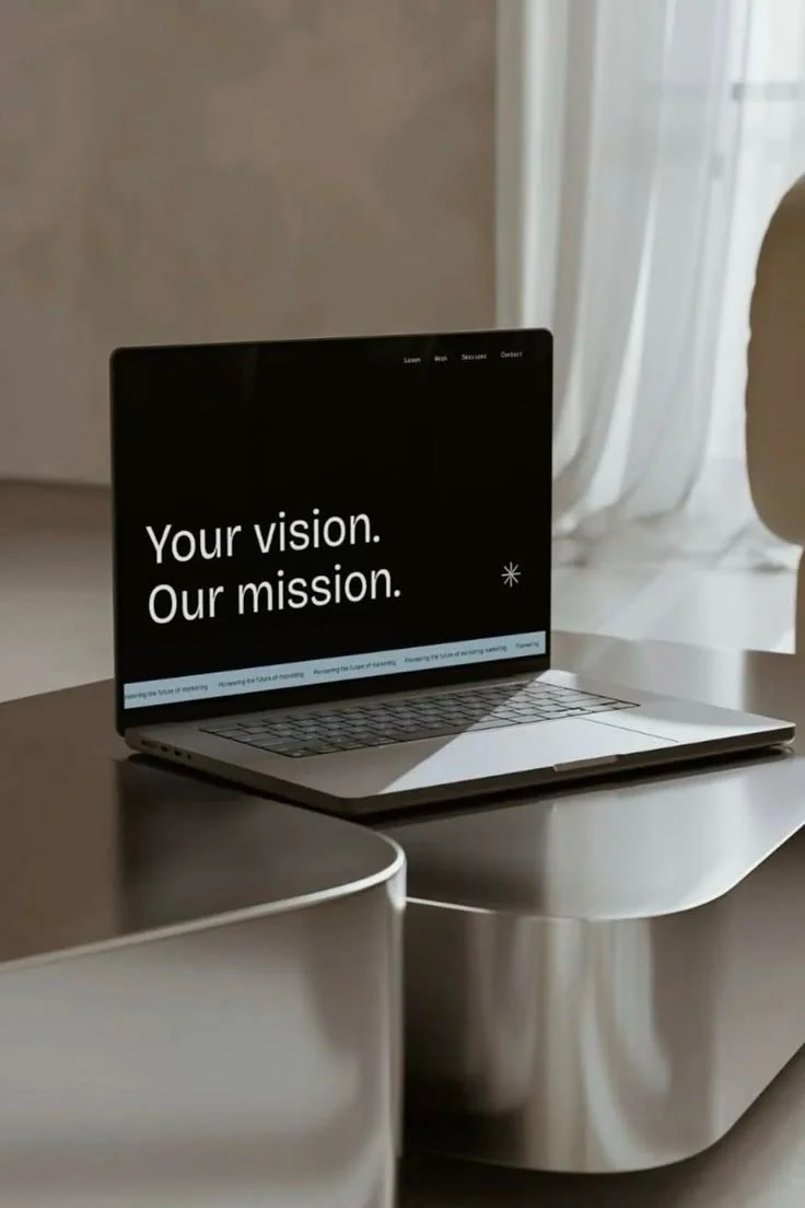 A silver laptop on a modern desk with the screen displaying the words 'Your vision. Our mission.' in white text.