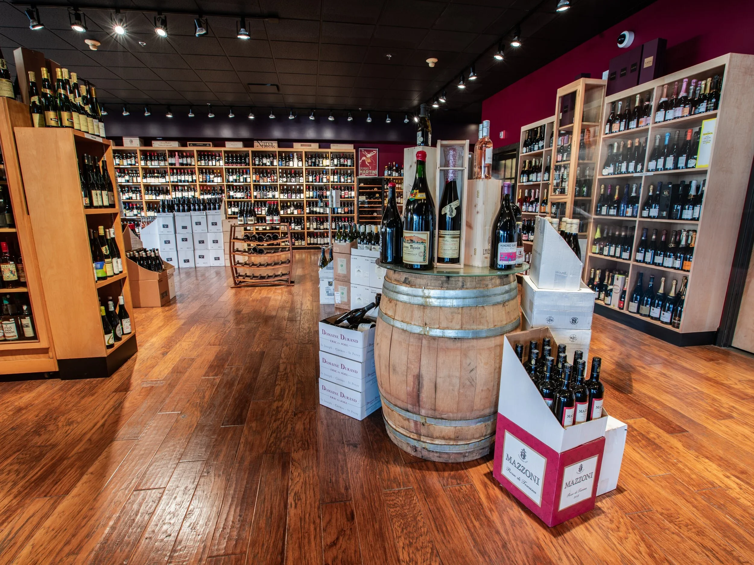 A wine store or wine shop with shelves of wine bottles, a barrel with bottles on top, and boxes of wine on a wooden floor and wall.