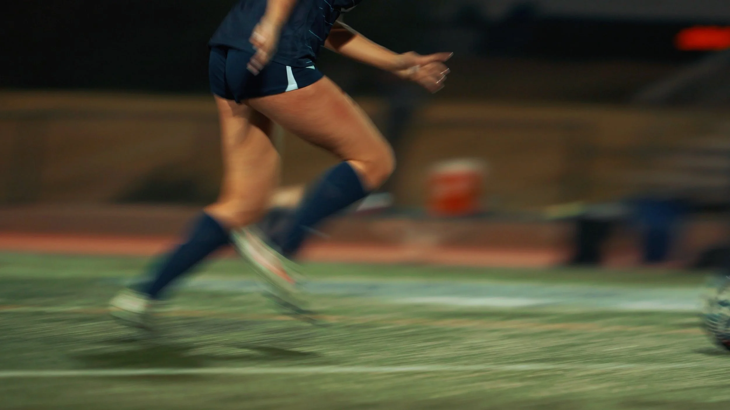 A person running on a track, wearing athletic clothing and shoes, captured in motion blur.
